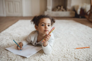 The Carpet Cleaners - adorable little african american girl drawing with pencils and lying on carpet at home