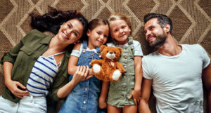 The Carpet Cleaners - Dad, mom and two lovely daughters are lying on the carpet on the floor in the living room. Happy family have fun together.
