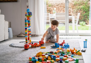 The Carpet Cleaners - Little toddler boy playing with Lego train blocks at home at quarantine isolation period during coronavirus pandemic. Child leisure activity, creative game, developing imagination and motor skills
