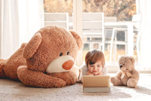 The Carpet Cleaners - Cute little child watching cartoons on digital tablet device lying on floor with two soft teddy bear toys at home. Modern childhood.